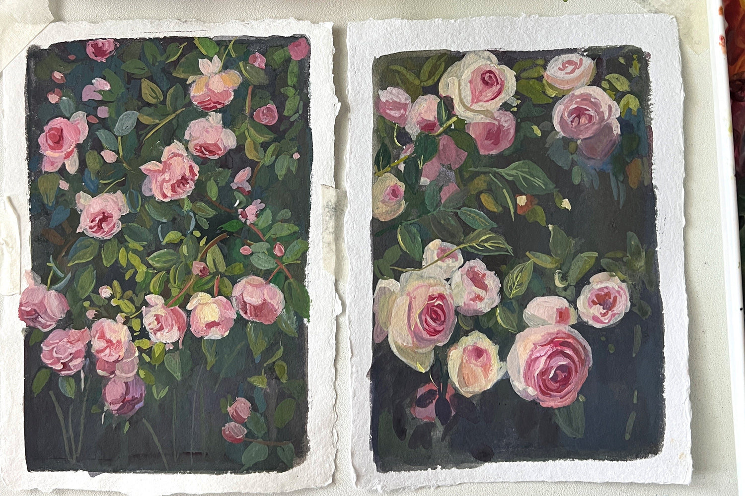 Two floral paintings on watercolor paper with a watercolor set and plant in the background.