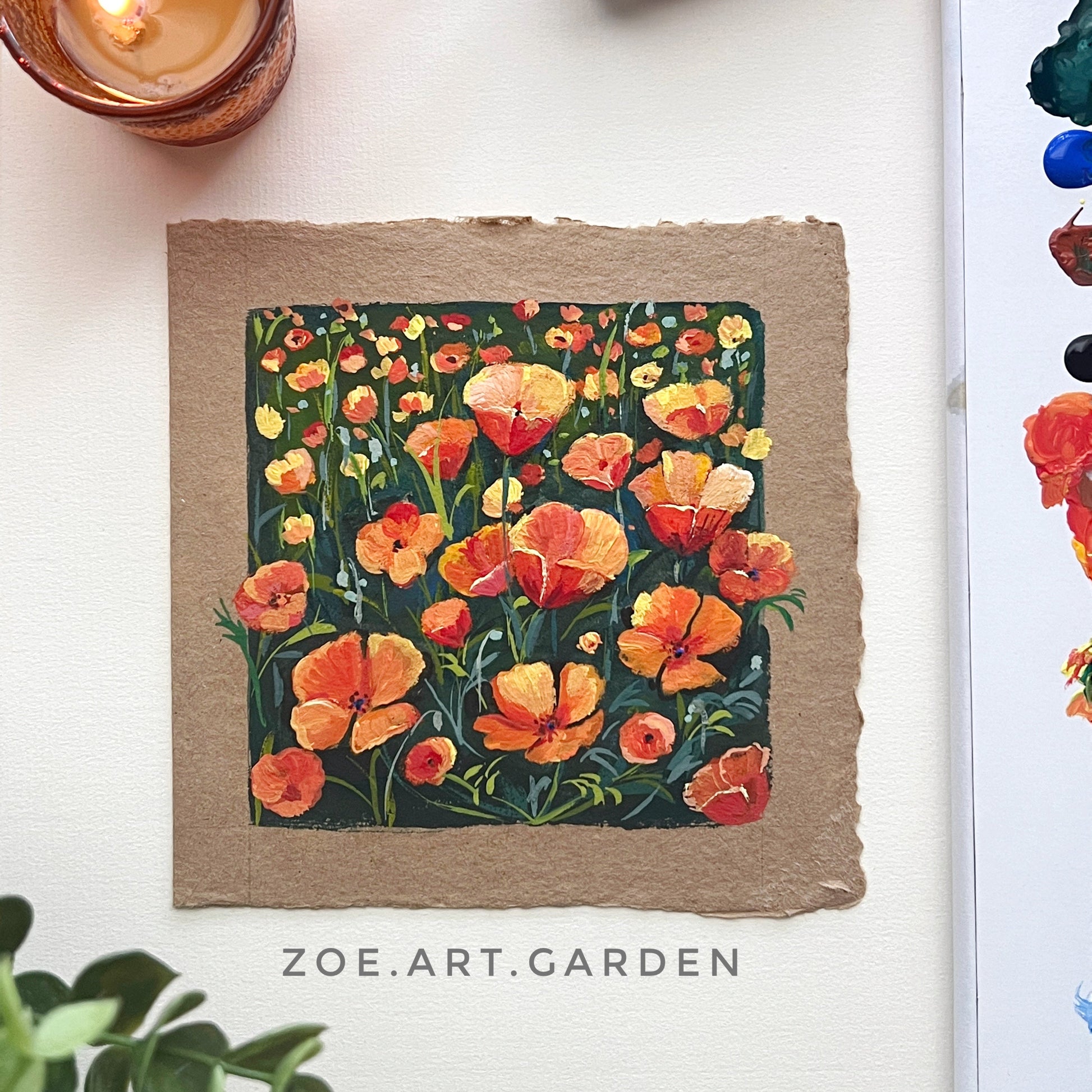 Floral painting on textured paper with two tubes of paint and a candle in the background.