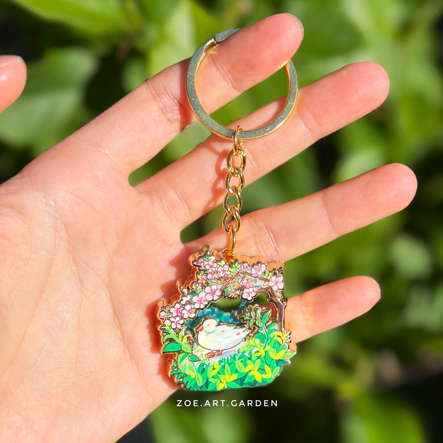 Colorful keychain with a design of a bird and flowers held in a hand against a green leafy background.