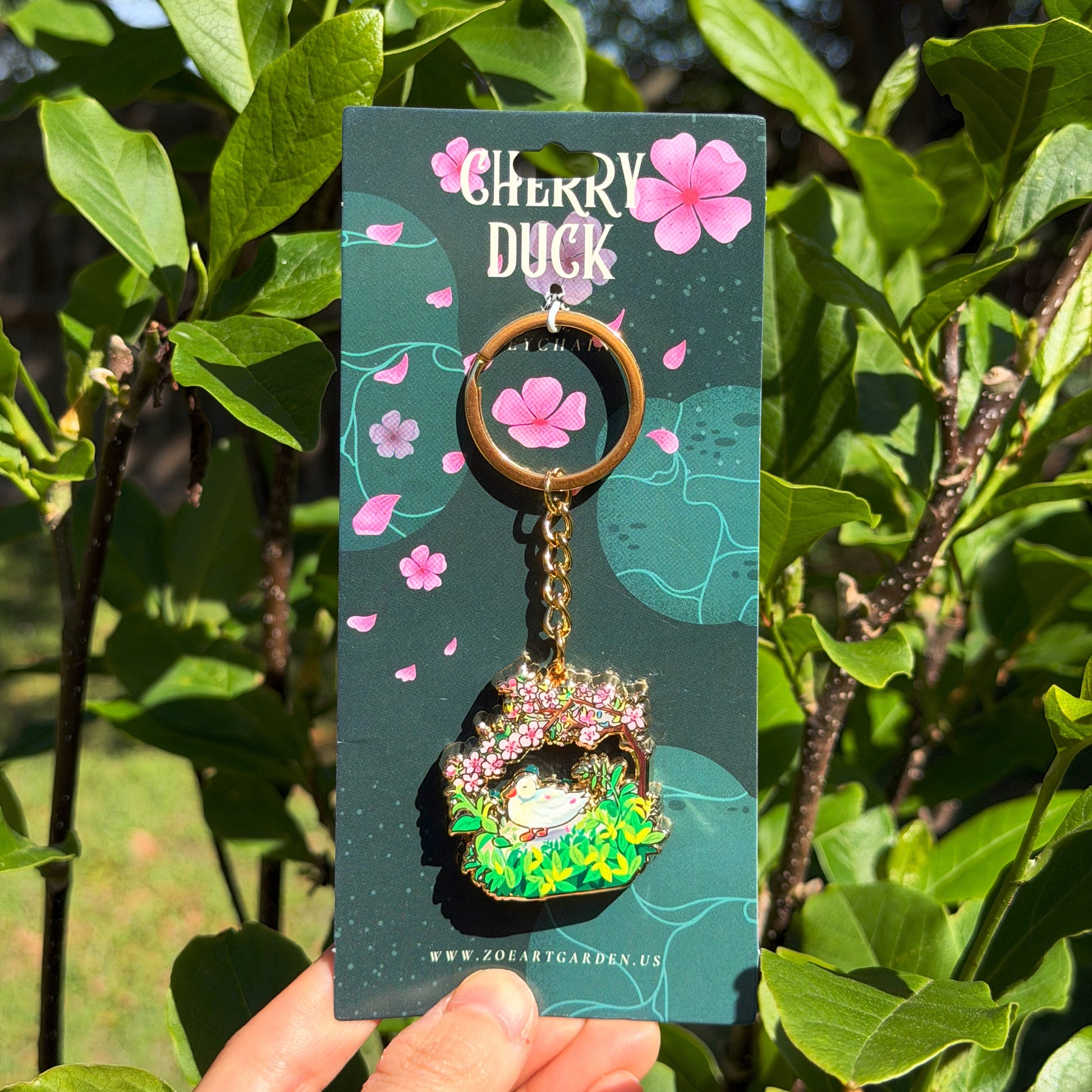 Keychain on a Cherry Duck branded card held in front of green foliage