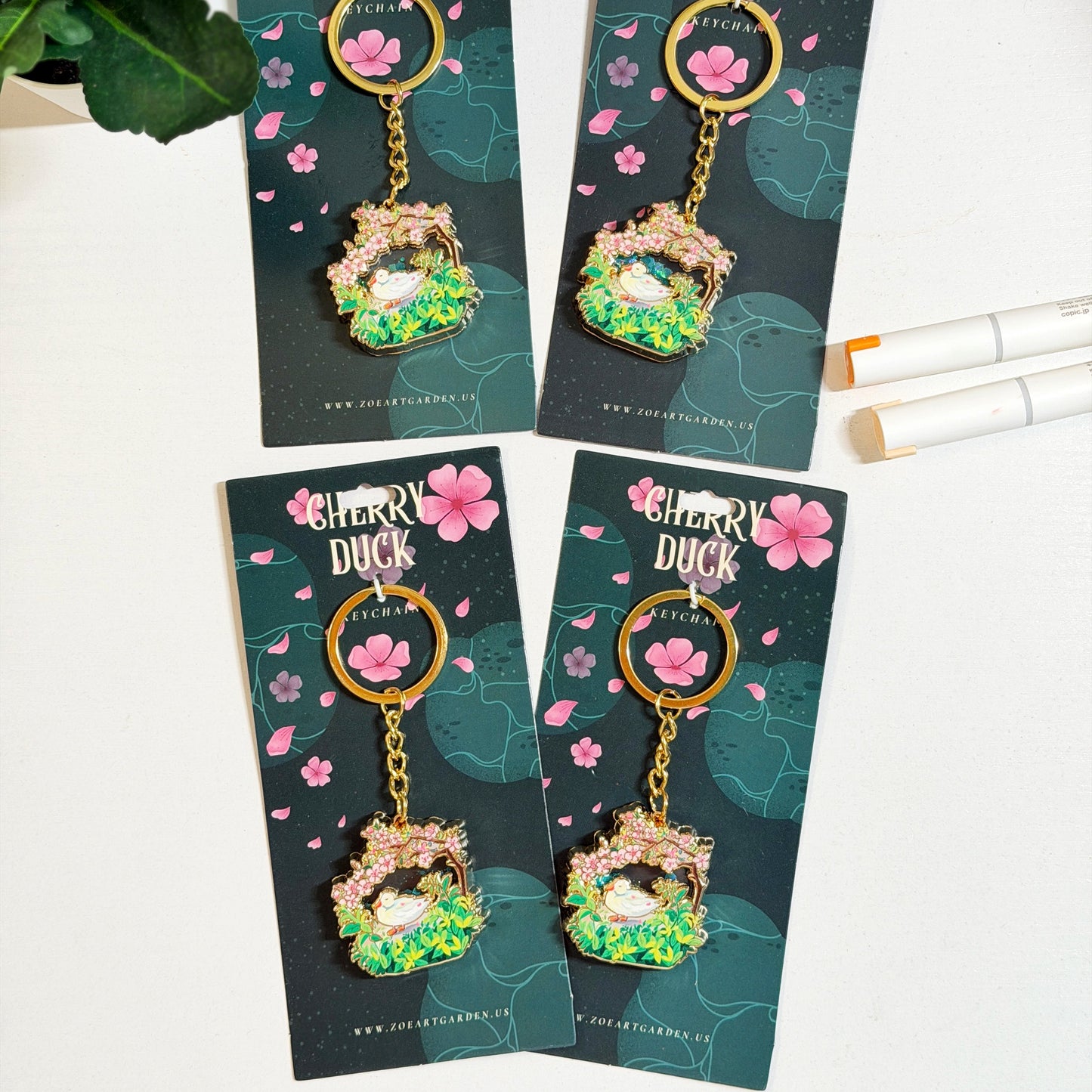 Cherry Duck keychains on green cards with floral design