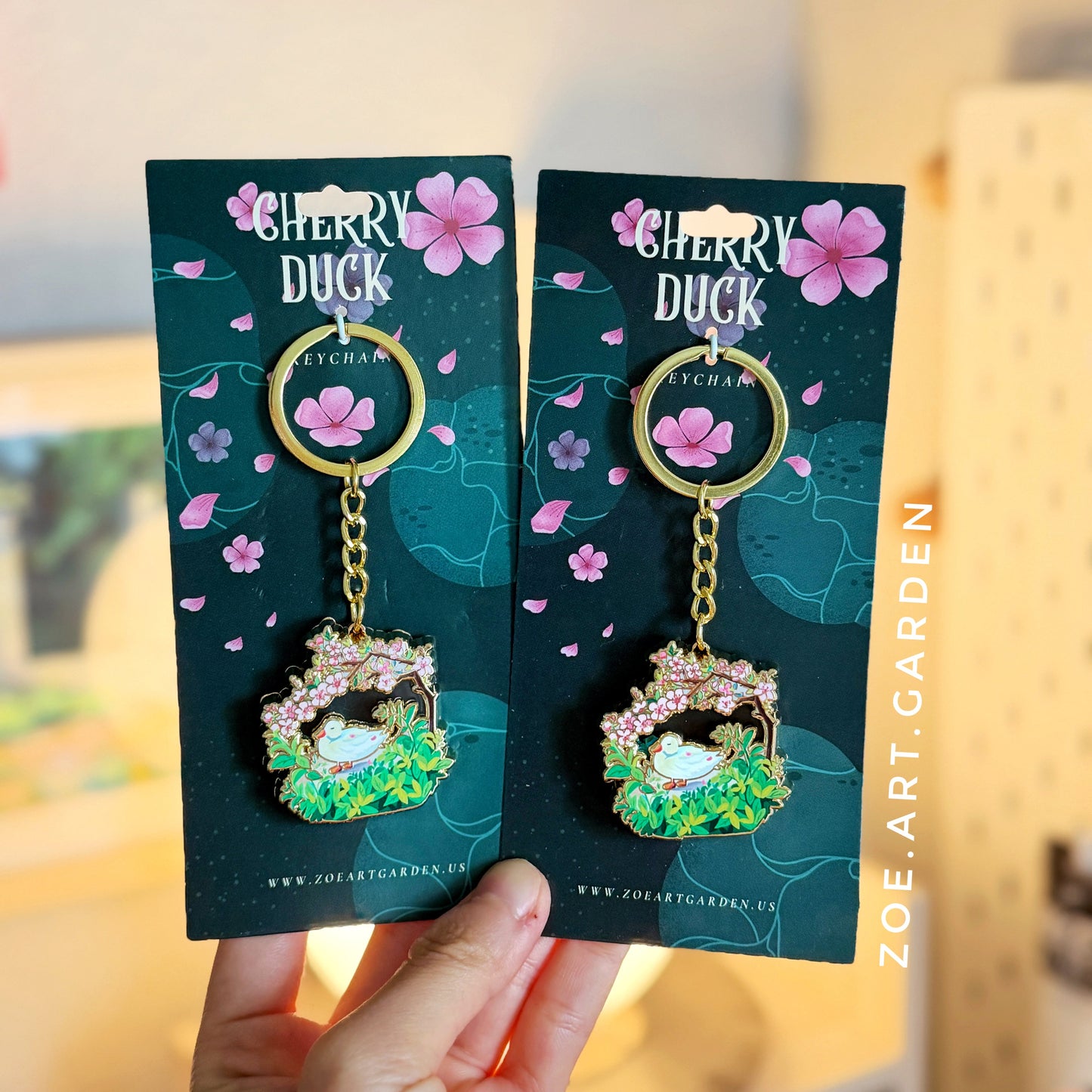 Cherry Duck keychains on packaging held by a hand with a blurred background