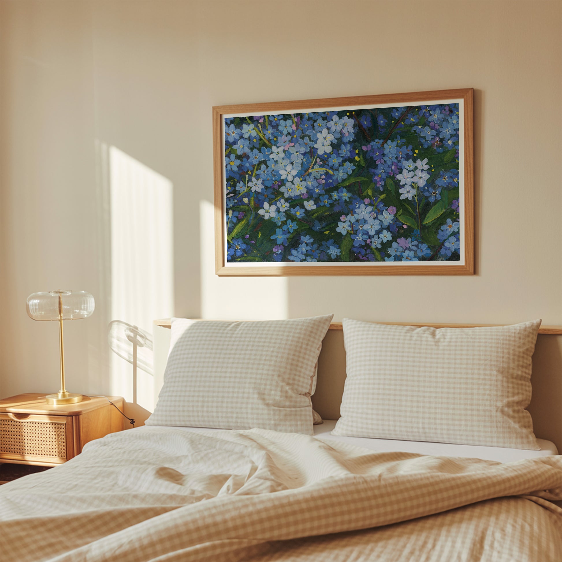 A framed floral painting with blue and white flowers hangs on a beige wall above a neatly made bed with beige checkered bedding and two pillows in a softly lit bedroom.