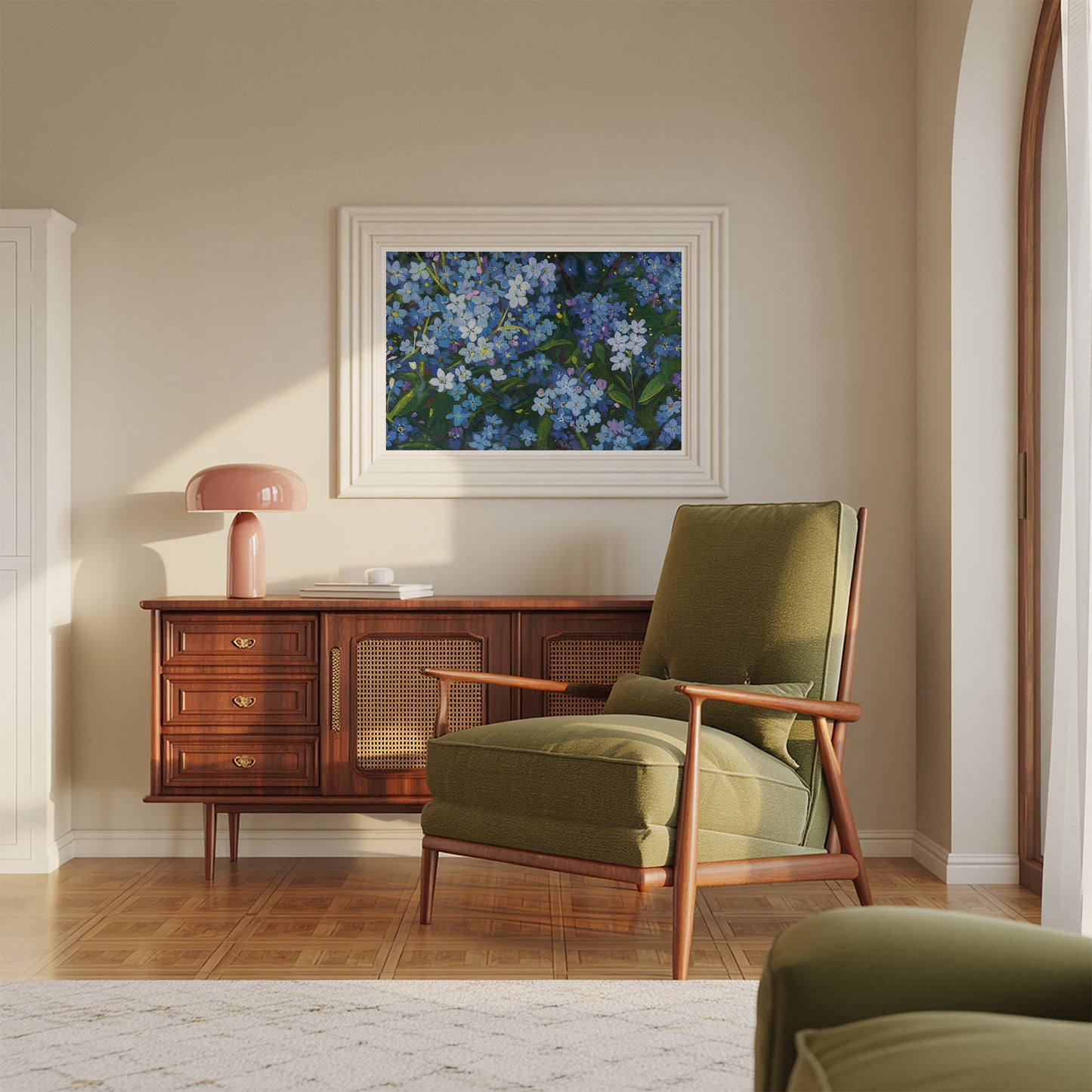 A framed floral art print featuring blue and white flowers hangs on a beige wall above a mid-century modern wooden credenza and olive green armchair in a sunlit room.