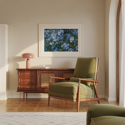 A framed floral art print featuring blue and white flowers hangs on a beige wall above a mid-century modern wooden credenza and olive green armchair in a sunlit room.