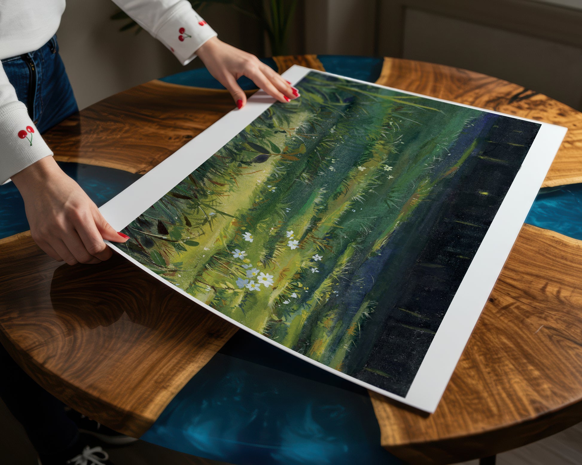 A person holds a large framed abstract landscape art print featuring green, yellow, and dark forest tones, displayed on a polished wooden table.