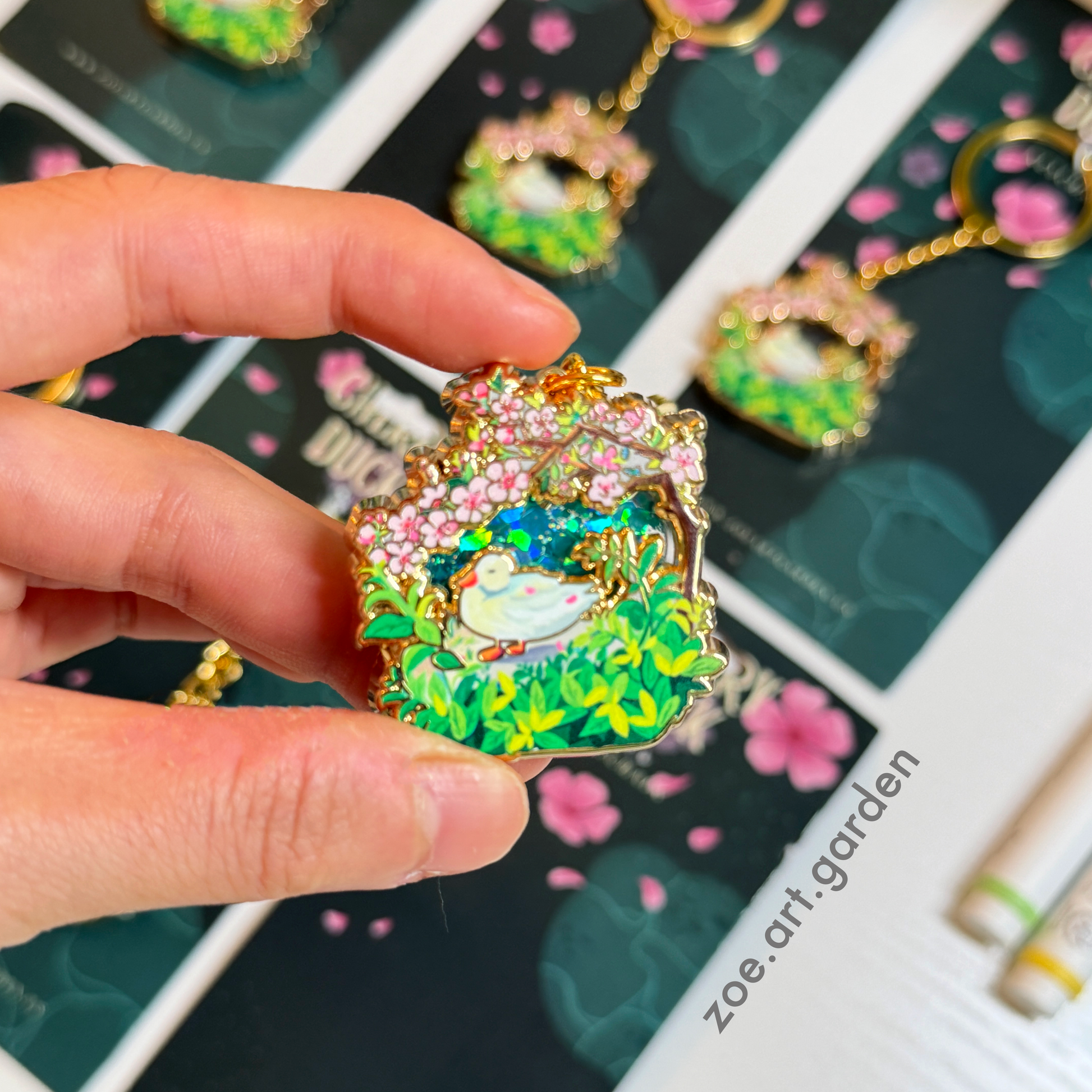 Hand holding a colorful keychain with a garden design, displayed against a background of similar keychains.