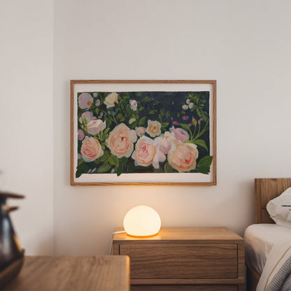 A framed floral painting featuring soft pink and cream roses with green leaves on a dark background, displayed on a white wall above a wooden nightstand with a glowing spherical lamp.