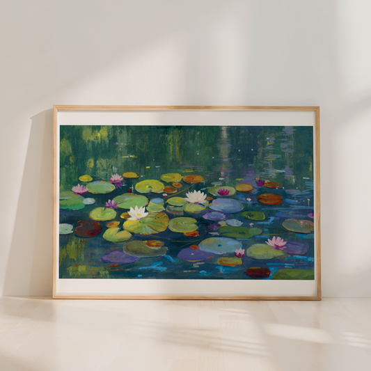 A framed painting of a pond with lily pads and water lilies in green, blue, yellow, pink, and white tones, leaning against a white wall on a light wood floor.